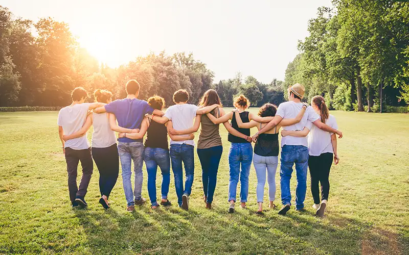 A group of people holding each others backs looking toward the sunset