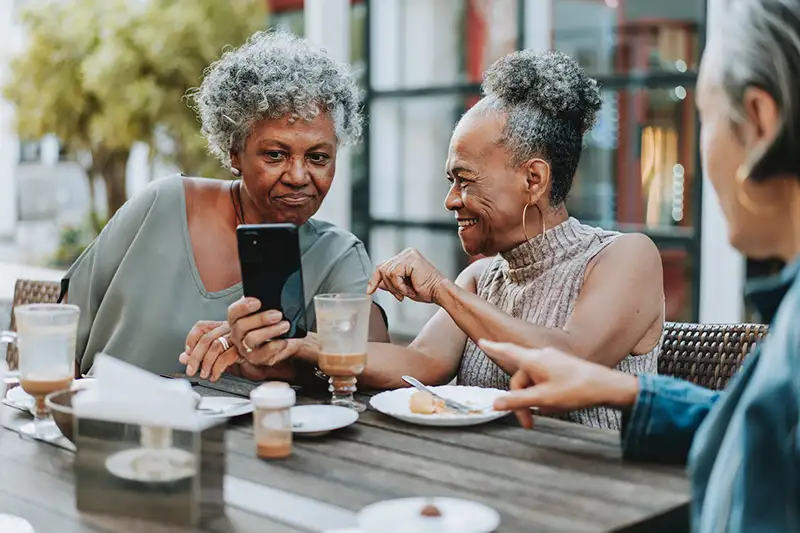 Two older women looking at a phone together while they have lunch