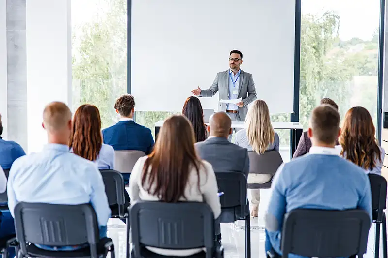 A man giving a speech at the front of a room while people listen