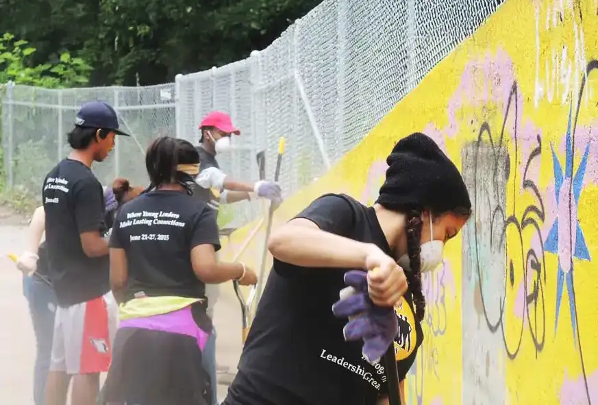 A group of young adults cleaning up graffiti on a city wall